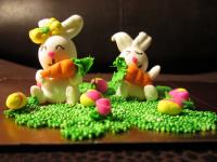 Rabbits holding carrots in the grass where there are easter eggs while flowers bloom